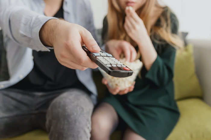 Man and woman watching tv and eating popcorn 