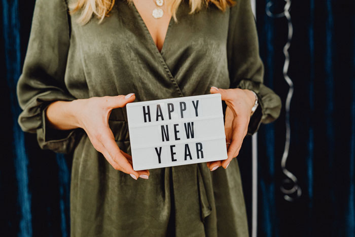 woman in a green dress holding a box with the words happy new year
