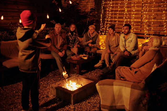 a group of people sitting around the fire and watching on boy who showing something