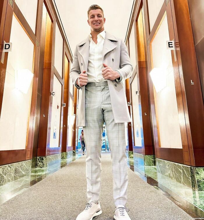 Man dressed in stylish coat and plaid pants standing in a hallway, representing smart celebrities known for intelligence.