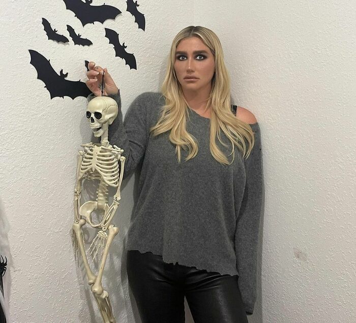 Woman posing with skeleton and black bat decorations on white wall, representing smartest celebrities and intelligence theme.