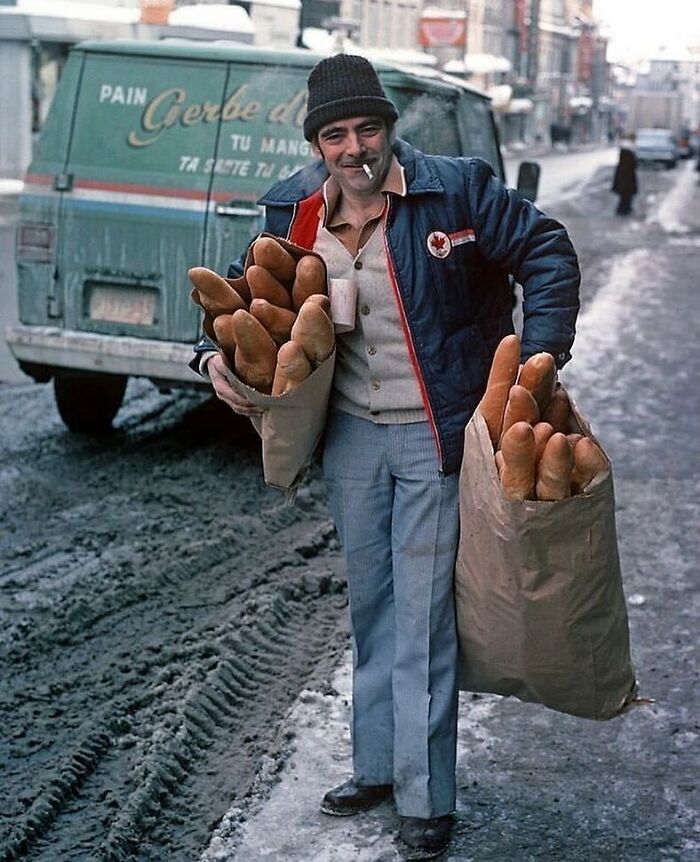 A Delivery Man With Bags Filled With Baguettes On A Snowy Street In Quebec, Canada, 1977