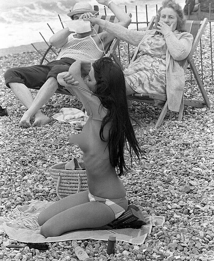 Woman Covering Man's Eyes With Her Knitting At Sight Of Young Woman Taking Off Her Top On The Beach, France, 1974