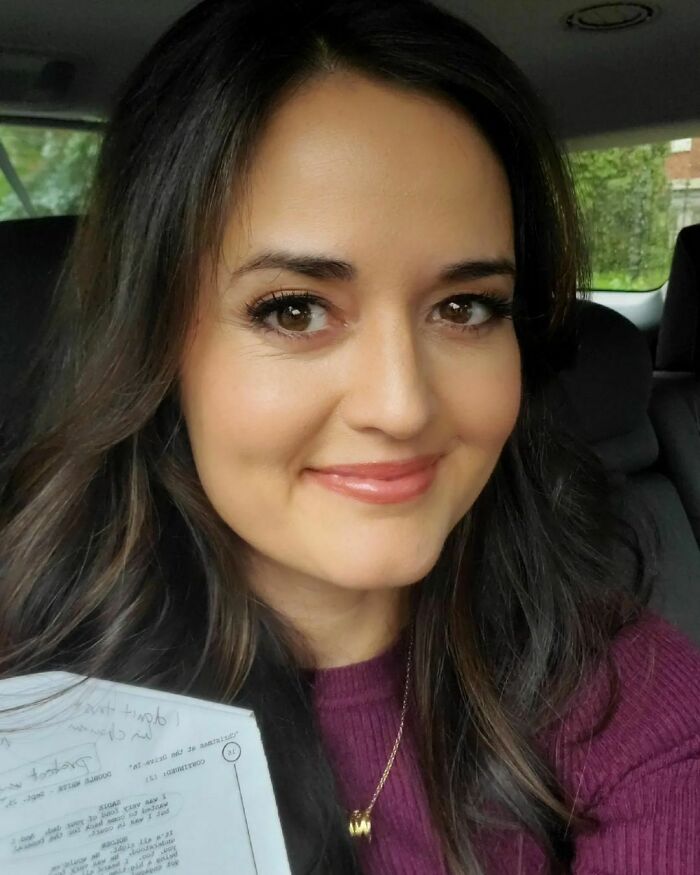 Woman with long dark hair holding a paper, smiling inside a car, representing smartest celebrities and intelligence.