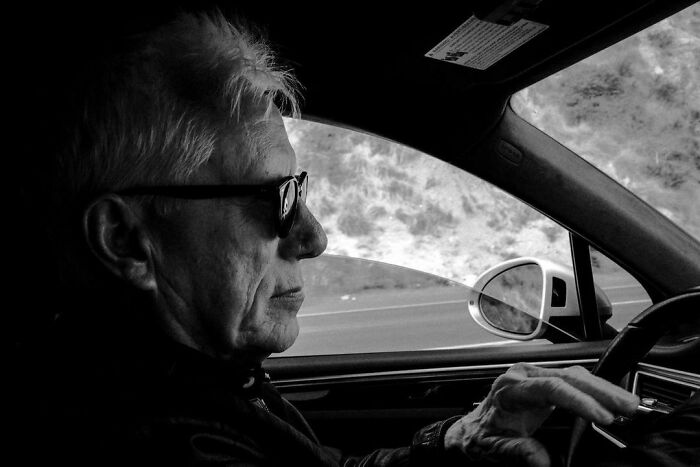 Older man wearing sunglasses driving a car, representing one of the smartest celebrities known for talent and intelligence.