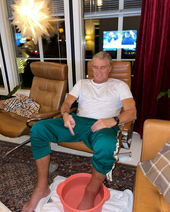 Man sitting barefoot in a living room soaking foot in a basin, illustrating relaxation of smartest celebrities and intelligent stars.