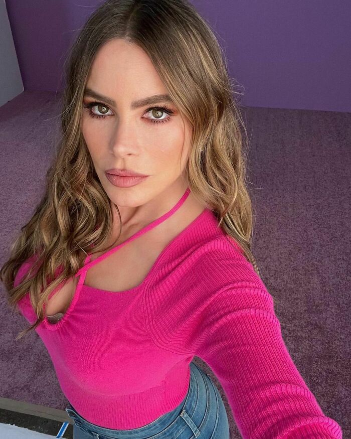 Celebrity wearing a pink top and jeans taking a selfie, representing smart celebrities known for talent and intelligence.