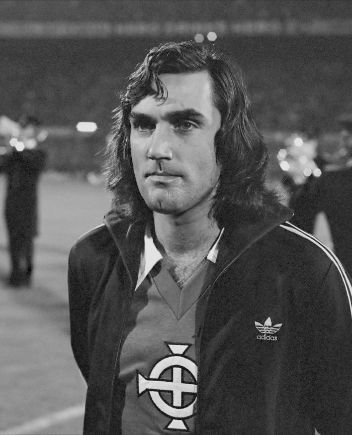 Black and white picture of George Best standing and watching
