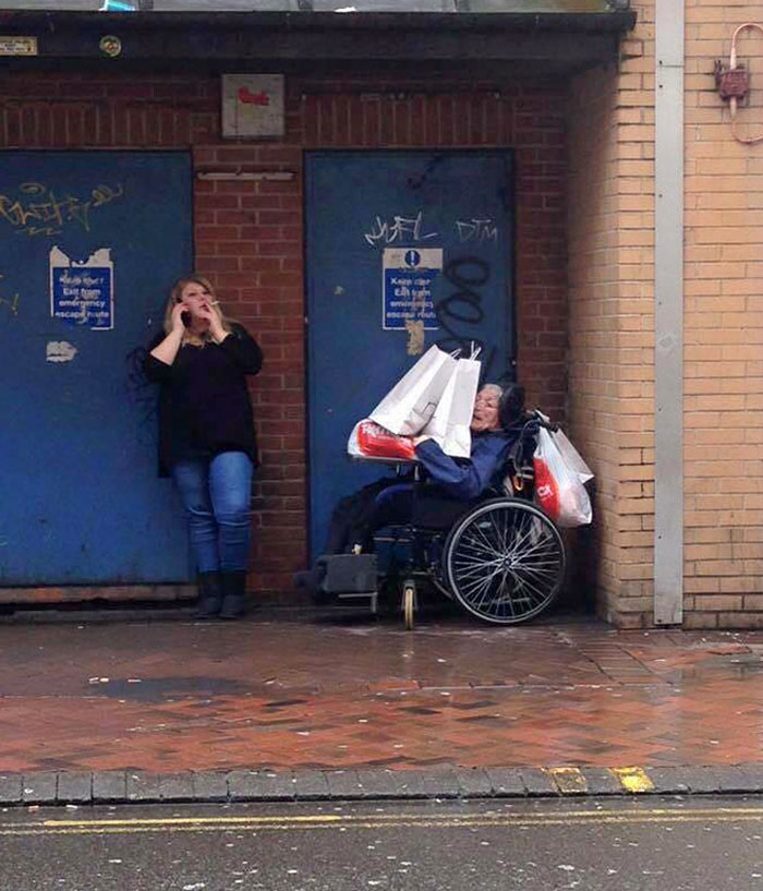Una cuidadora deja las bolsas de las compras sobre la persona discapacitada que tiene a su cargo para poder tomar un descanso y poder fumar 