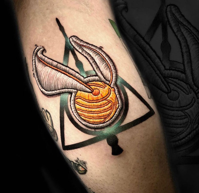 Harry Potter tattoo featuring a golden snitch and triangle symbol on arm, in vibrant colors.
