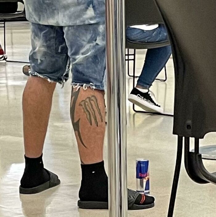 Funny brand loyalty tattoo on calf, featuring a logo, with a can of energy drink on the floor nearby.