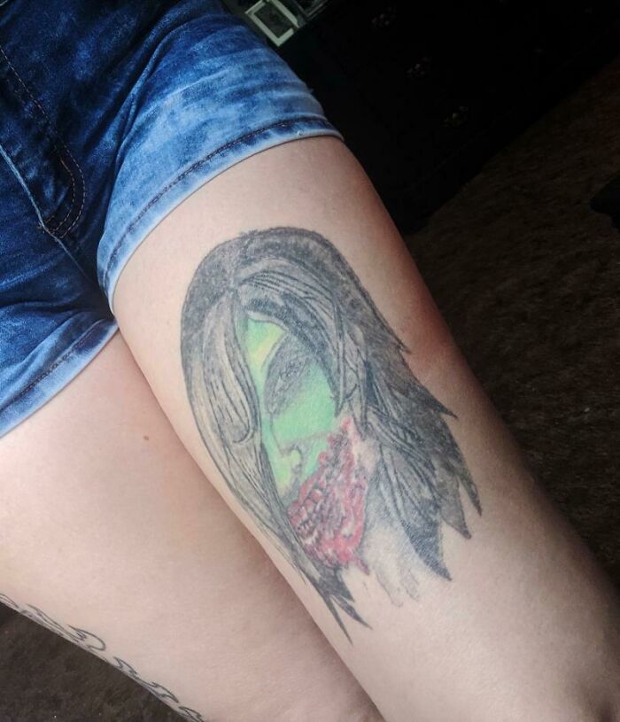 Thigh tattoo of a humorous zombie face design in green and red, creating a funny tattoo look.