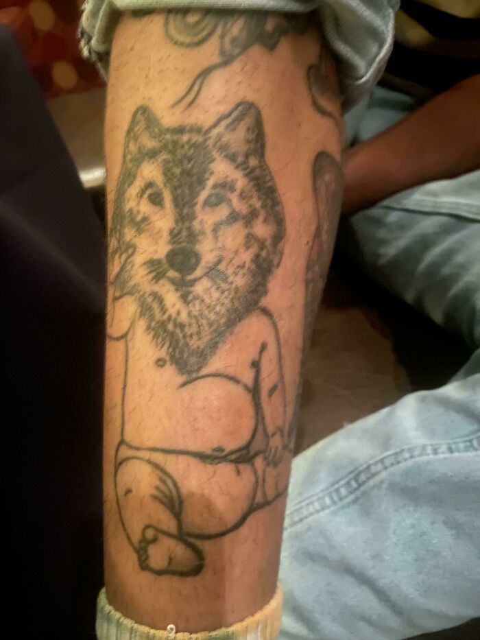 Funny tattoo of a chubby baby with a wolf's head on a person's leg, designed to evoke humor.
