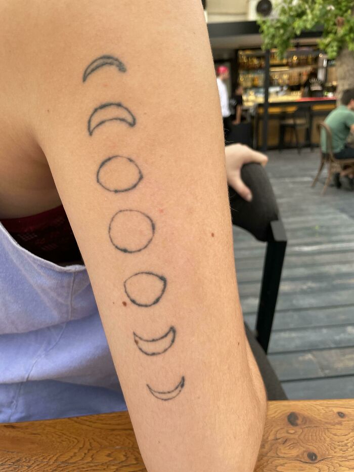 Arm with funny tattoo of incomplete circle patterns, casually displayed at an outdoor café setting.