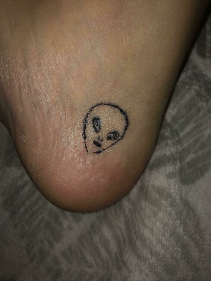 Funny tattoo of a small alien face on a heel.