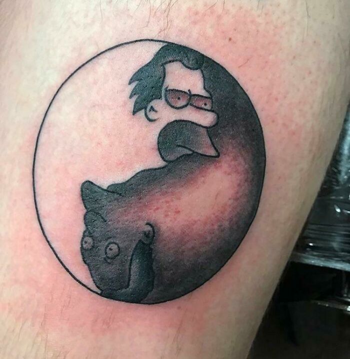 Cartoon-inspired funny tattoo featuring stylized animal and person within a yin-yang design.