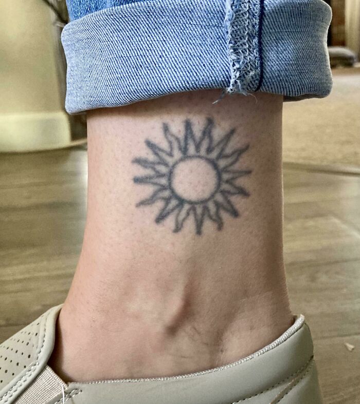 Aged tattoo of a sun on an ankle, faded over time, showcasing how tattoos change after years.