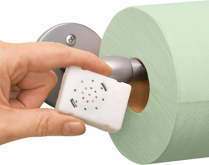 Person holding a small white device near a green toilet roll 