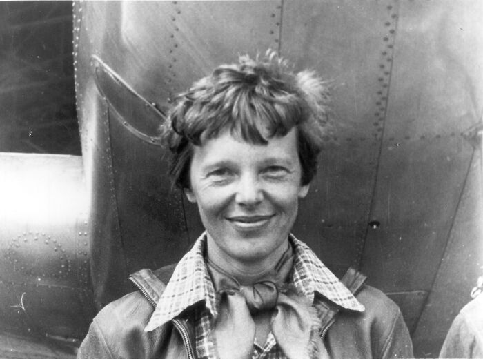 Amelia Earhart standing under nose of her Lockheed Model 10-E Electra. Gelatin silver print, 1937