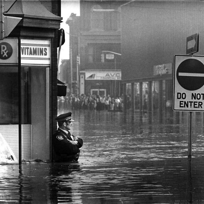 Agente de policía vigilando una farmacia en una zona inundada, Ontario, 1974