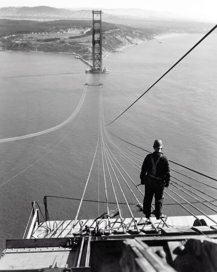 Un hombre de pie sobre los primeros cables durante la construcción del puente Golden Gate, con el Presidio y San Francisco al fondo. 1935