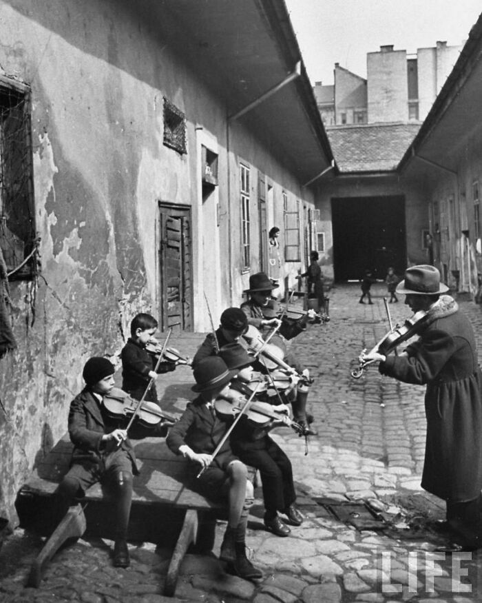 Niños gitanos aprendiendo a tocar el violín en el patio de una de las casas más pobres. Budapest, Hungría, 1939 por William Vandivert