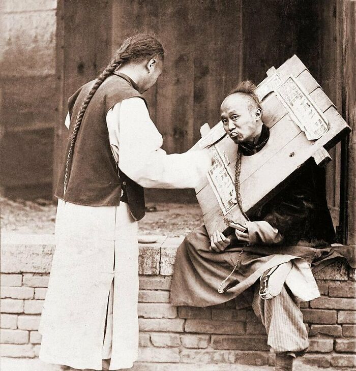 Charitable Chinese Man Feeding A Criminal In A Cangue. Ca. 1905