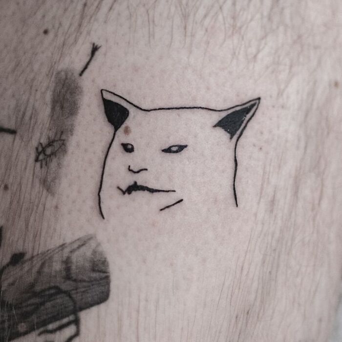 Funny tattoo of an unimpressed cat face on pale skin.