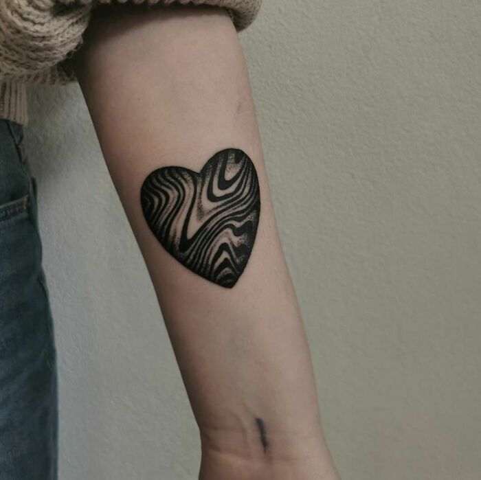 Heart-shaped optical illusion tattoo with wavy patterns on forearm.