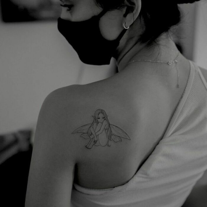 Celebrity tattoo of a fairy on a Camila Mendes's shoulder, wearing a mask and tank top, in a monochrome setting.