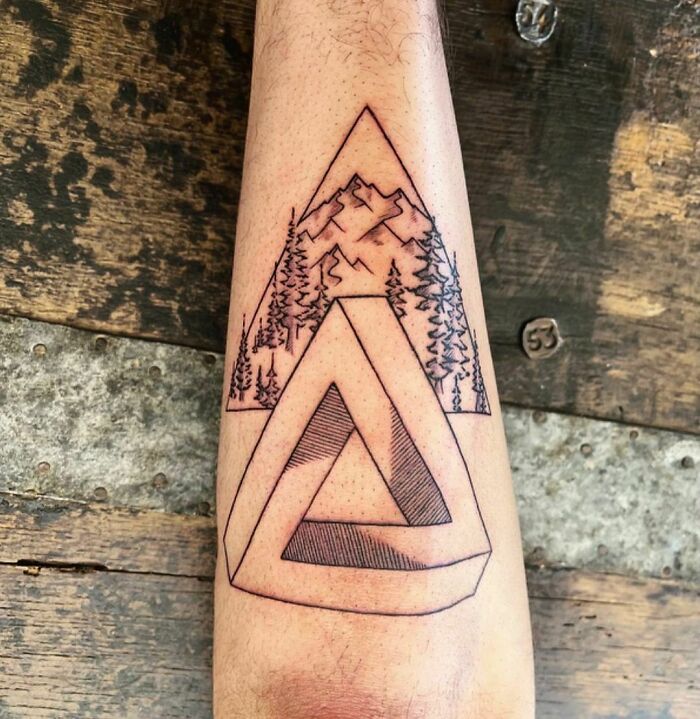 Optical illusion tattoo of a geometric shape blending into a mountain landscape on an arm.
