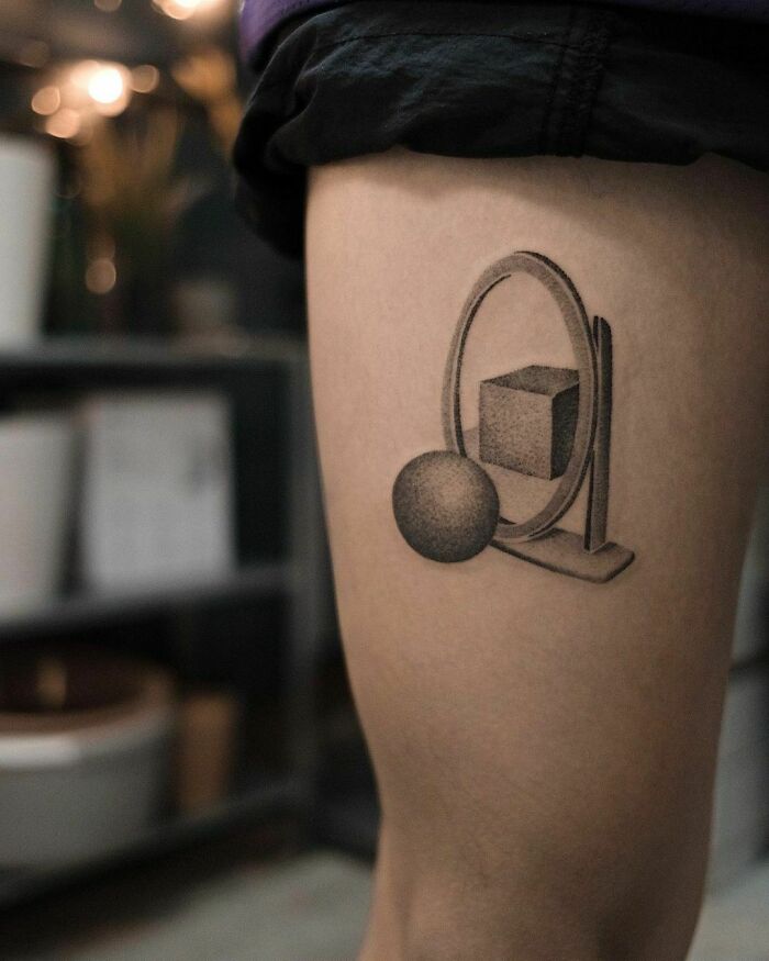 Optical illusion tattoo of a 3D sphere and cube design on a person's leg.