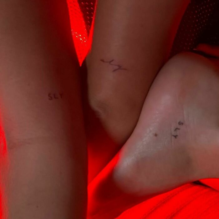 Three small celebrity tattoos on skin with red lighting, featuring simple text designs.