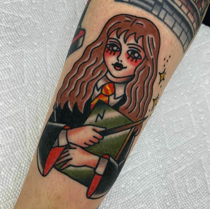 Harry Potter tattoo featuring a witch with long hair, wand, and book, wearing a school uniform with red and gold tie.