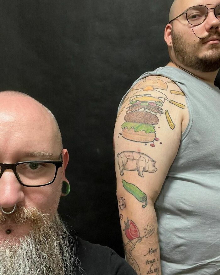 Two people with funny tattoos, including a burger and food items, on one man's arm, humorously displayed.