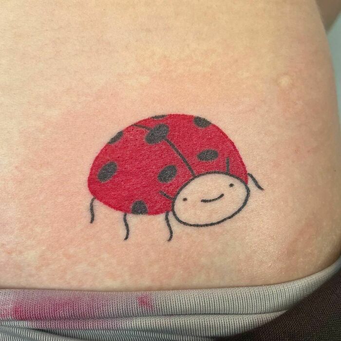 Cute and funny ladybug tattoo with a smiling face on skin.