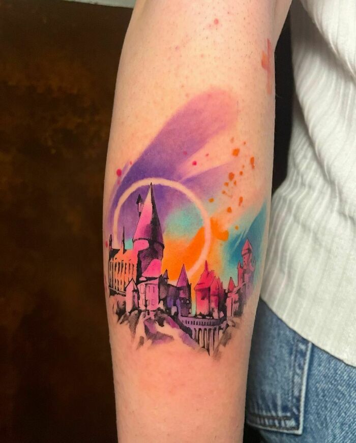 Colorful Hogwarts tattoo on arm, representing Harry Potter, with vibrant purple, orange, and blue watercolor design.