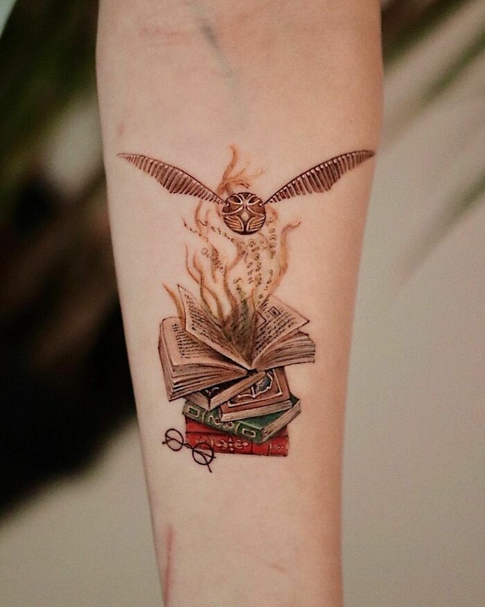 Harry Potter tattoo of the Golden Snitch flying above magical books and glasses.