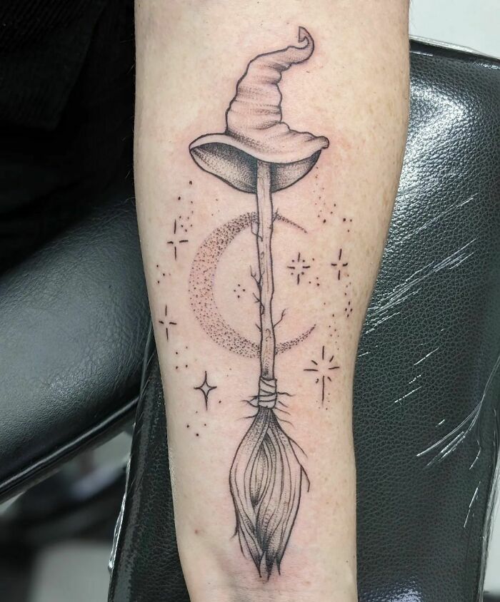 Harry Potter tattoo of a broomstick with a wizard hat and celestial accents on an arm.