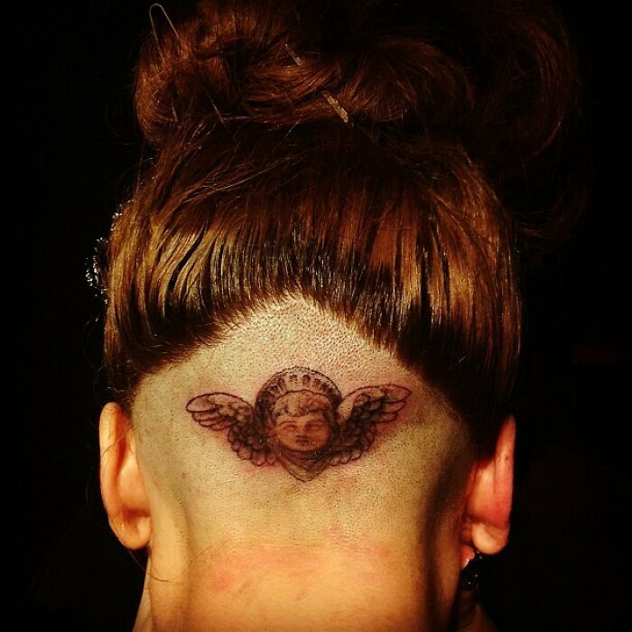 Angel tattoo on the back of a person's shaved head, showcasing celebrity tattoo art.