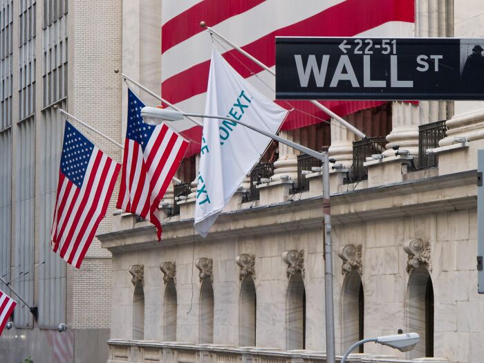 Sign of wall street and multiple flags behind the sign 