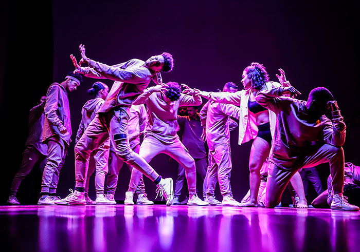 Group of dancers performing on stage with dynamic poses under purple lighting, highlighting big trends in dance styles.