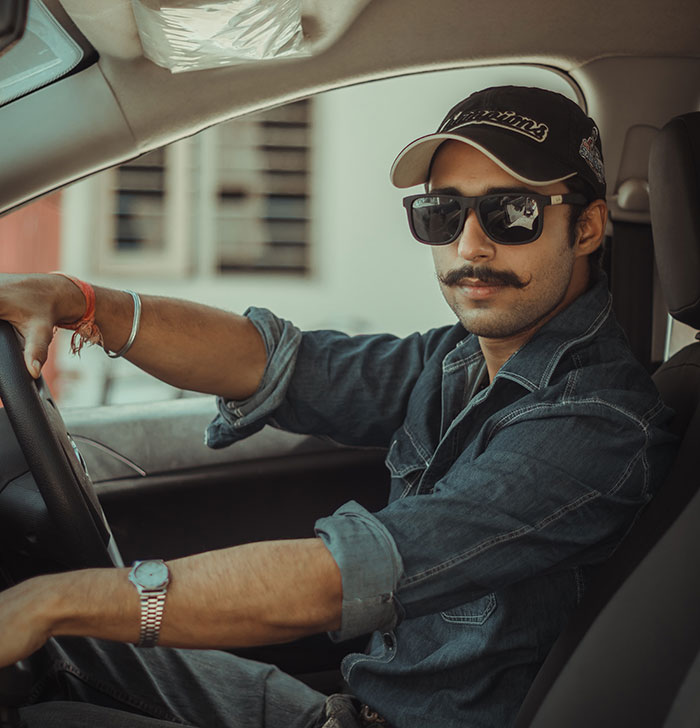 Man wearing sunglasses and a cap, sitting in a car, representing retro big trends in fashion and style.