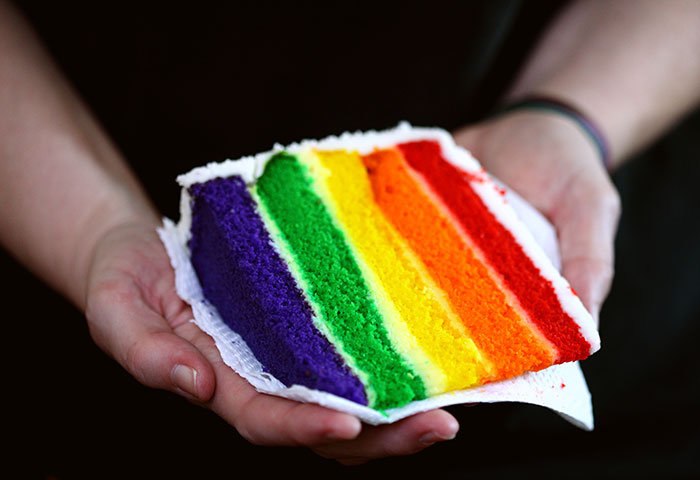 Hands holding a colorful rainbow layered cake slice, highlighting vibrant big trends in nostalgic and forgotten styles.