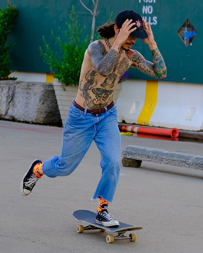 Skateboarder with tattoos wearing a black cap and blue jeans shows big trends in urban street style.