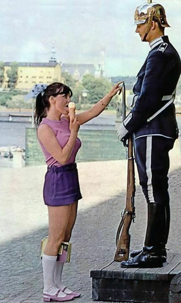 1970. Chica lamiendo helado y jugando con la punta de la bayoneta del arma para provocar la reacción de un guardia real en el exterior del Palacio de Estocolmo, Estocolmo, Suecia