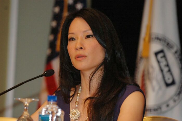 Lucy Liu wearing a purple dress speaking at a panel, representing celebrities who never married yet found love.
