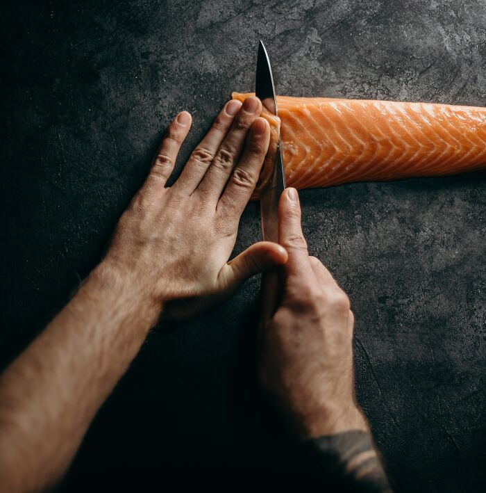 Kitchen Chef Slicing Salmon With A Knife 