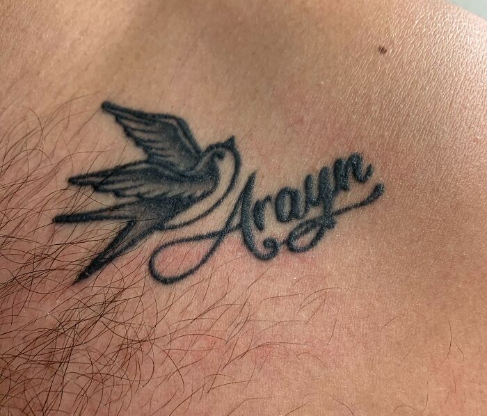 Funny tattoo featuring a swallow and the name "Aroyn" in cursive on skin.