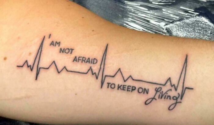 Arm tattoo with heartbeat line and the phrase "I am not afraid to keep on living."